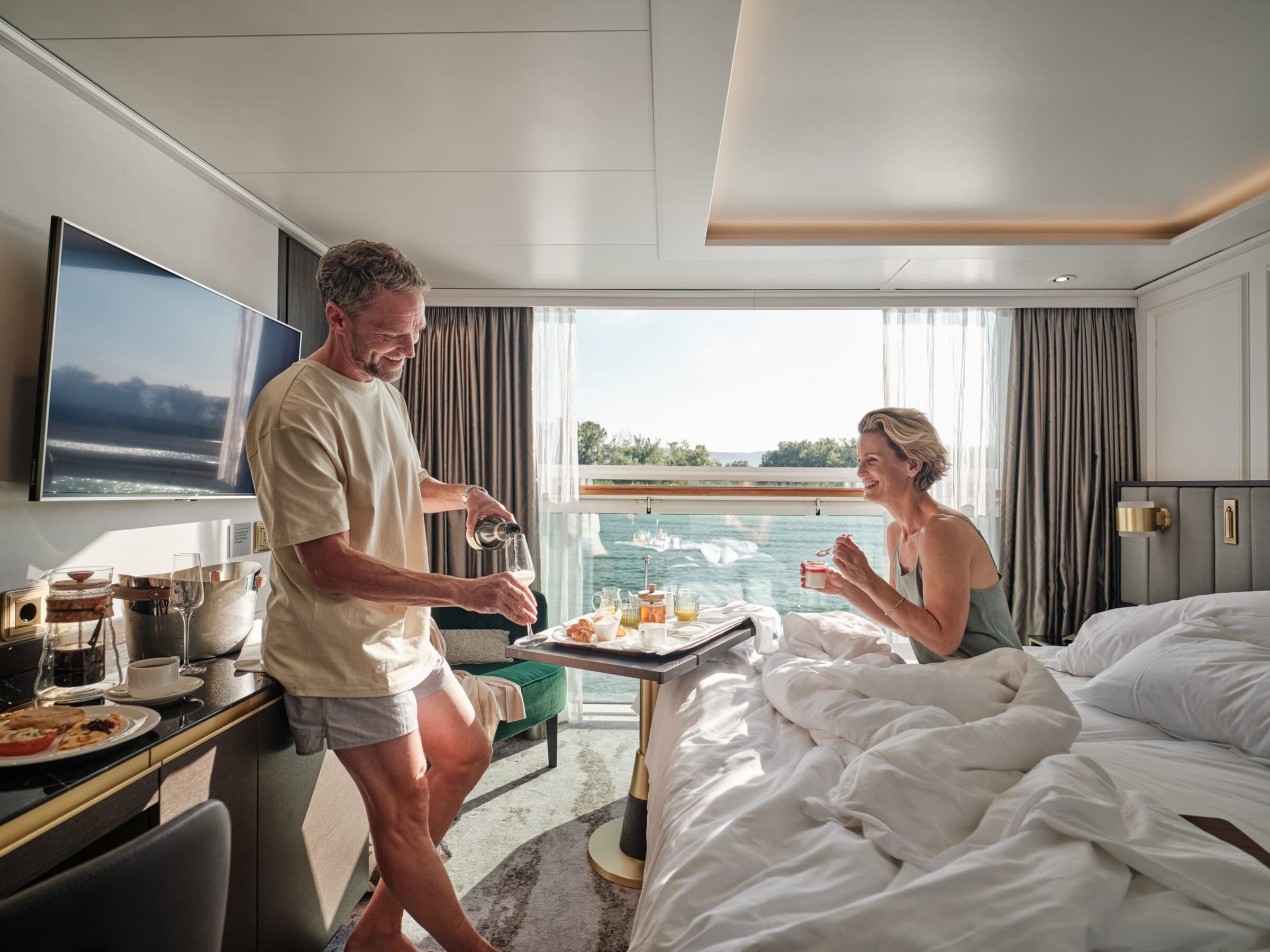 couple enjoying breakfast in their river cruise cabin w a view of the water outside