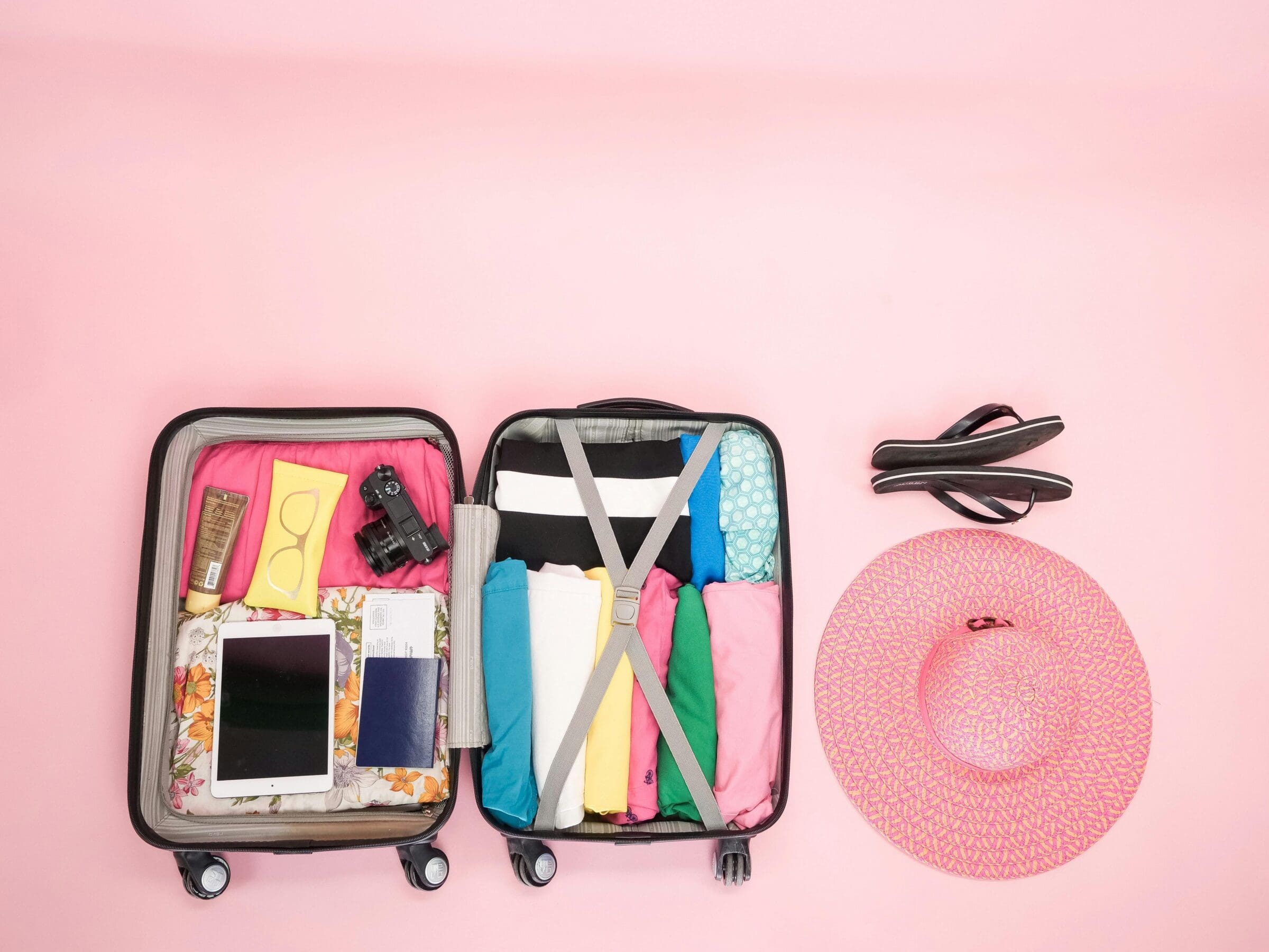 open suitcase on a pink background with pink hat to the side