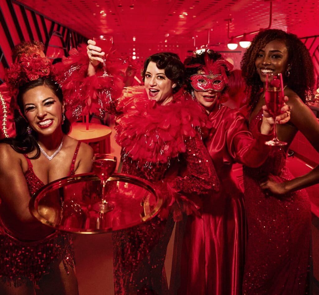 4 women in red in a red room with drinks in hand celebrating women traveling together