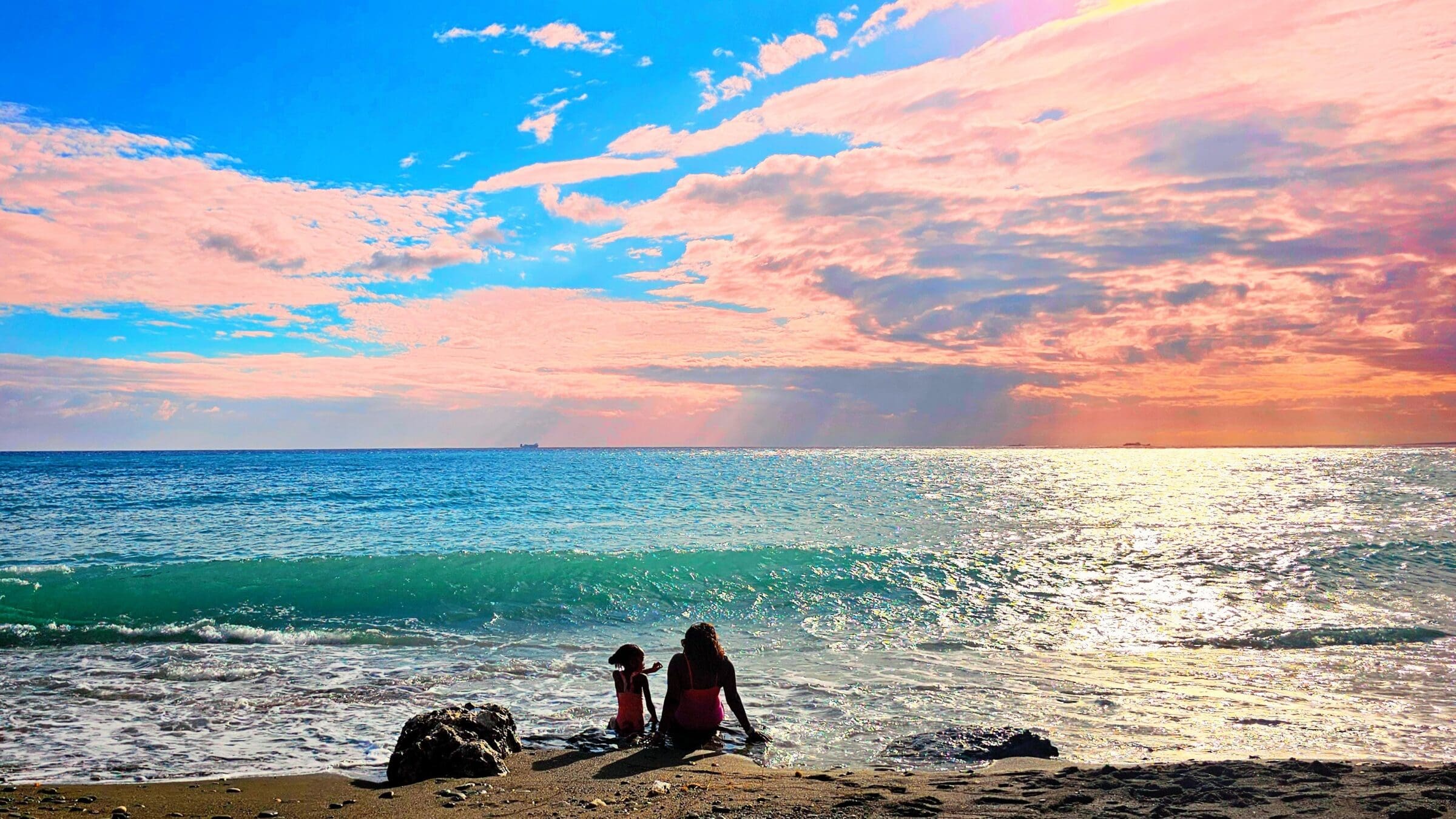 mom and child sit on rock at oceans edge in Jamaica