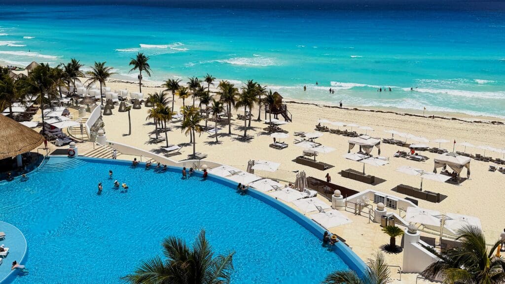 Views of the pool, beach with palm trees, umbrellas and loungers and ocean at Le Blanc Spa resort Cancun.