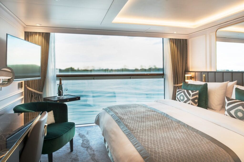 River cruise cabin w bed, chair tv desk and floor to ceiling window vies of the river