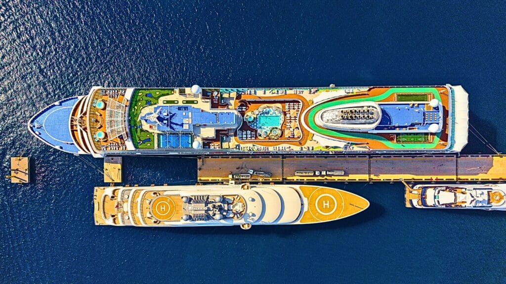 Top-down view of two luxurious cruise ships moored at a sunny port, showcasing pools and helipads.