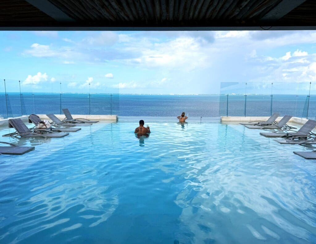2 people in an infinity pool look out at the clear blue ocean